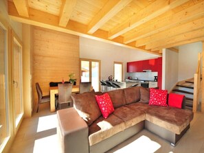 A modern living room with a large sectional sofa, a dining area, and a kitchen with red cabinets. - Chalet Ourson Blanc by Interhome (Hérémence)