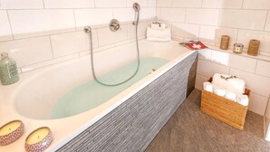 A bathroom with a glass-enclosed bathtub, white tiled walls, a wooden ceiling, and a wicker basket with towels. - Chalet des Etoiles by Interhome (Hérémence)