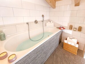 A bathroom with a glass-enclosed bathtub, white tiled walls, a wooden ceiling, and a wicker basket with towels. - Chalet des Etoiles by Interhome (Hérémence)