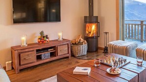 A cozy living room with a fireplace, a television, a chessboard, and a dining table. - Chalet des Etoiles by Interhome (Hérémence)