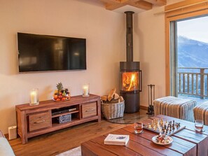 A cozy living room with a fireplace, a television, a chessboard, and a dining table. - Chalet des Etoiles by Interhome (Hérémence)