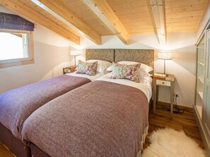Een slaapkamer met twee bedden, houten balken in het plafond, een raam met gordijn en bedlampen.