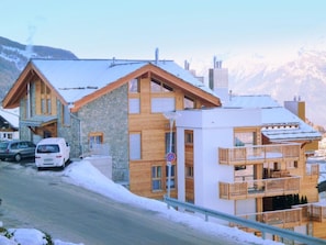 A multi-story wooden building with balconies, a stone facade, and a snowy mountain backdrop. - Ski Heaven Veysonnaz by Interhome (Veysonnaz)