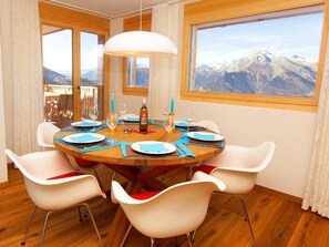 A dining room with a wooden table set for six, white chairs, a chandelier, and a mountain view. - Ski Heaven Veysonnaz by Interhome (Veysonnaz)