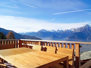 Eine Holzdiele mit Tisch und Stühlen, mit Blick auf eine gebirgige Landschaft.