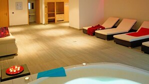 Ett spa-rum med ett bubbelbad, solstolar, ett träskåp och ett litet bord med ljus.