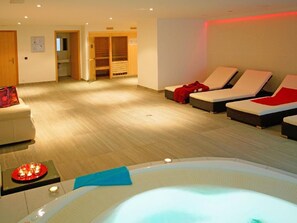 Ein Wellnessraum mit Whirlpool, Liegestühlen, einer Holzkabine und einem kleinen Tisch mit Kerzen.
