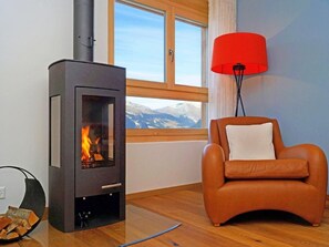 Ein Zimmer mit Kaminofen, Ledersessel, roter Stehlampe und Fenster mit Blick auf die Berge.