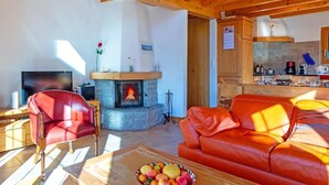 Uma sala de estar acolhedora com lareira, um sofá de couro vermelho, uma televisão e uma mesa de jantar com frutas.