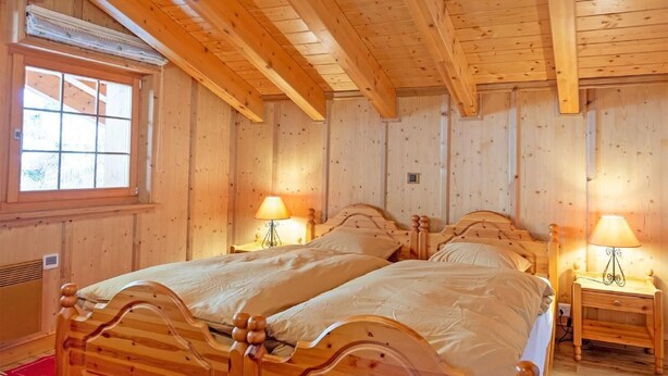 Um quarto com painéis de madeira, duas camas de madeira, uma janela e duas luminárias de cabeceira.