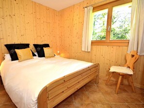 Quarto com painéis de madeira, uma cama, almofadas, uma mesa de cabeceira e uma janela com cortinas.