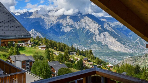 A mountain view from a wooden balcony overlooking a valley with houses and a clear sky. - Chalet Pierina by Interhome (La Tzoumaz)