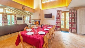 A dining area with a long table set for a meal, wooden chairs, a fireplace, and large windows. - Chalet Pierina by Interhome (La Tzoumaz)