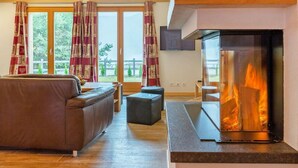 A modern living room with a fireplace, wooden ceiling beams, and large windows. - Chalet Pierina by Interhome (La Tzoumaz)