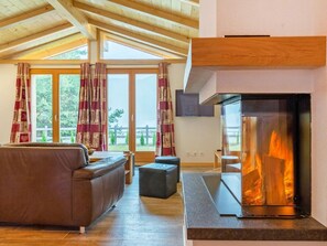 A modern living room with a fireplace, wooden ceiling beams, and large windows. - Chalet Pierina by Interhome (La Tzoumaz)