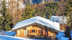 A wooden cabin with a snow-covered roof, surrounded by a forested mountain landscape. - Chalet Pierina by Interhome (La Tzoumaz)