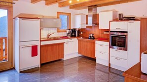 A modern kitchen with wooden beams, white cabinets, a stainless steel oven, and a coffee maker. - Chalet Julia by Interhome (La Tzoumaz)