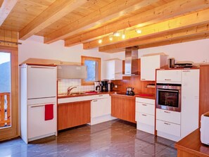 A modern kitchen with wooden beams, white cabinets, a stainless steel oven, and a coffee maker. - Chalet Julia by Interhome (La Tzoumaz)