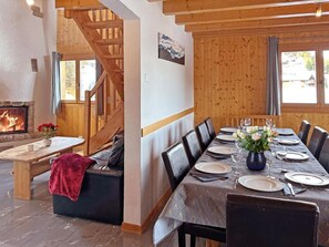 Ein Essbereich mit einem langen Tisch, gedeckt für sechs Personen, Holzwänden, einem Kamin und einer Treppe.