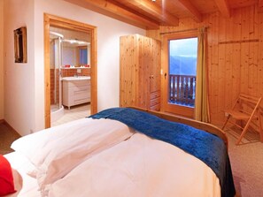 Ein Schlafzimmer mit einem großen Bett, einem Holzschrank, einem Badezimmer mit einem Waschbecken und einem Balkon mit Blick.