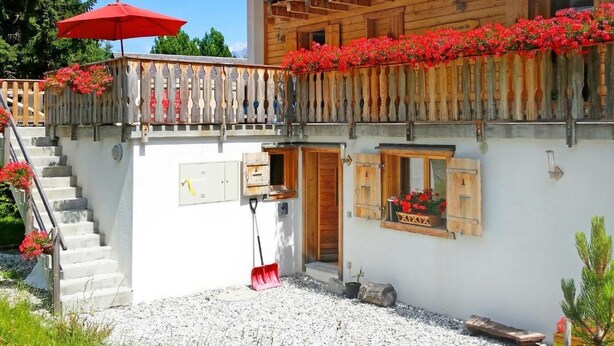 En stuga av trä med en balkong som är prydd med röda blommor, en trappa som leder upp till entrén och en skylt som visar att det är ”Chalet Châtillon”.