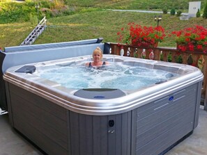 Ein Whirlpool mit einer Person darin, umgeben von einer Holzterrasse und einem Garten mit roten Blumen.