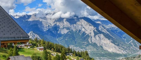 A mountain view from a wooden balcony overlooking a valley with houses and a clear sky.