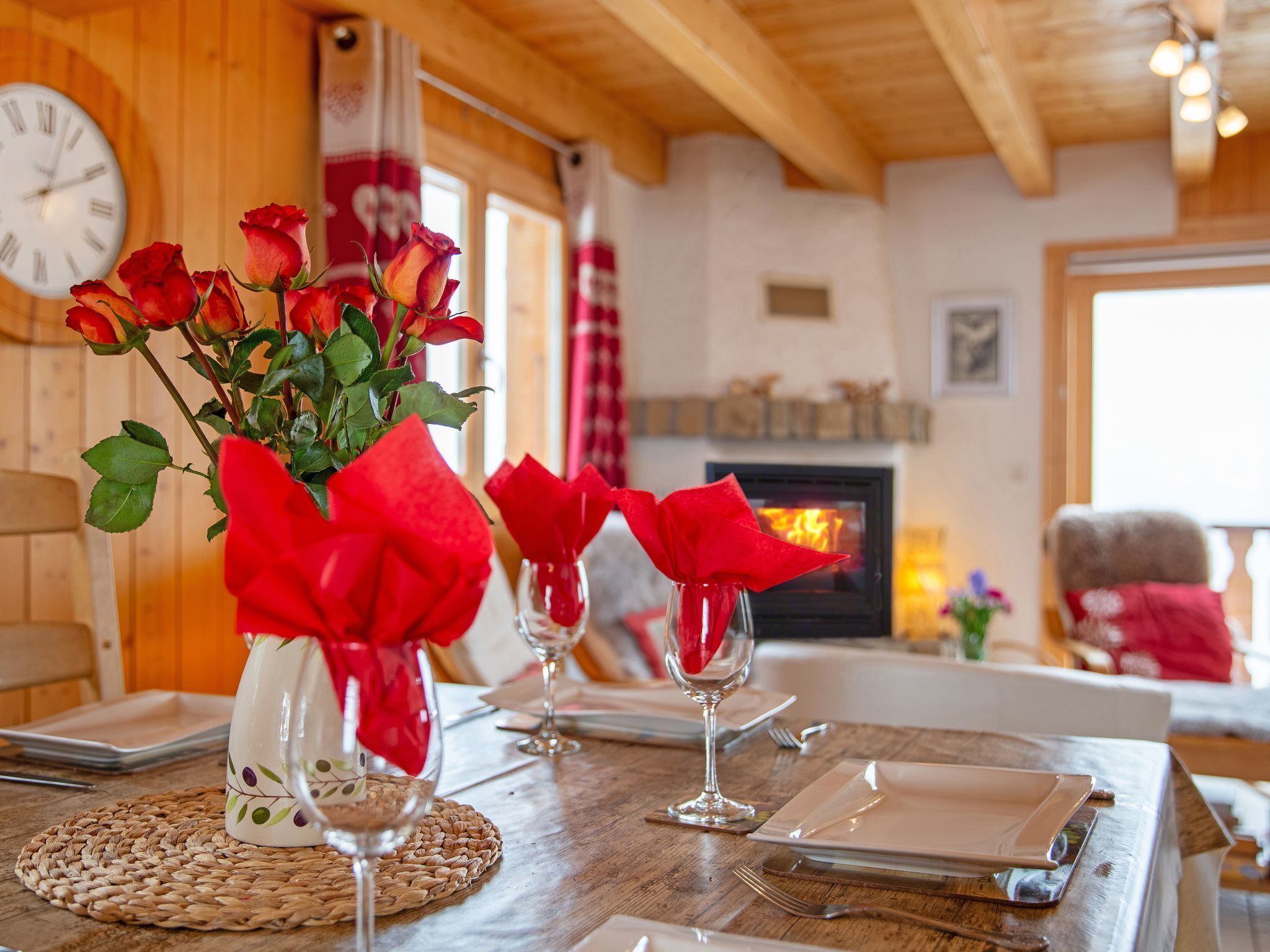 Une table à manger dressée avec un vase de roses rouges, des verres à vin et des couverts.