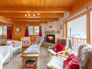 A cozy living room with wooden walls and ceiling, a fireplace, and a view of the outdoors. - Chalet Charmille by Interhome (La Tzoumaz)