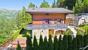 Un chalet con balcón, base de piedra y vistas a las montañas circundantes.