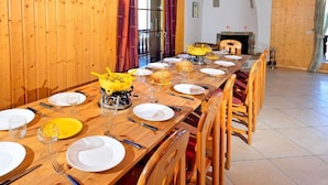 Una mesa de comedor de madera preparada para una comida, con sillas, chimenea y vistas al exterior.