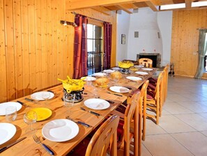 Ein Esszimmer mit Holztisch, gedeckten Plätzen, Stühlen, Kamin und Blick ins Freie.