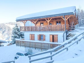 A two-story wooden chalet with balconies, wooden railings, and a snowy mountain backdrop. - Chalet Maria by Interhome (La Tzoumaz)