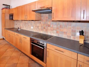 A kitchen with wooden cabinets, a stainless steel range hood, a double oven, and a tiled backsplash. - Chalet Maria by Interhome (La Tzoumaz)