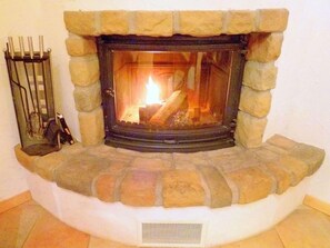 A stone fireplace with a fire burning inside, a metal screen, and a vent at the bottom. - Chalet Maria by Interhome (La Tzoumaz)