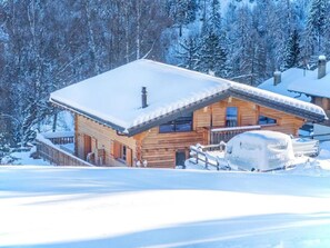 Eine Holzhütte mit schneebedecktem Dach, eingebettet in eine verschneite Landschaft mit Bäumen.