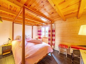 A wooden four-poster bed with a canopy, a bedside table, a chair, and a window with curtains. - Quatre Vallees by Interhome (La Tzoumaz)