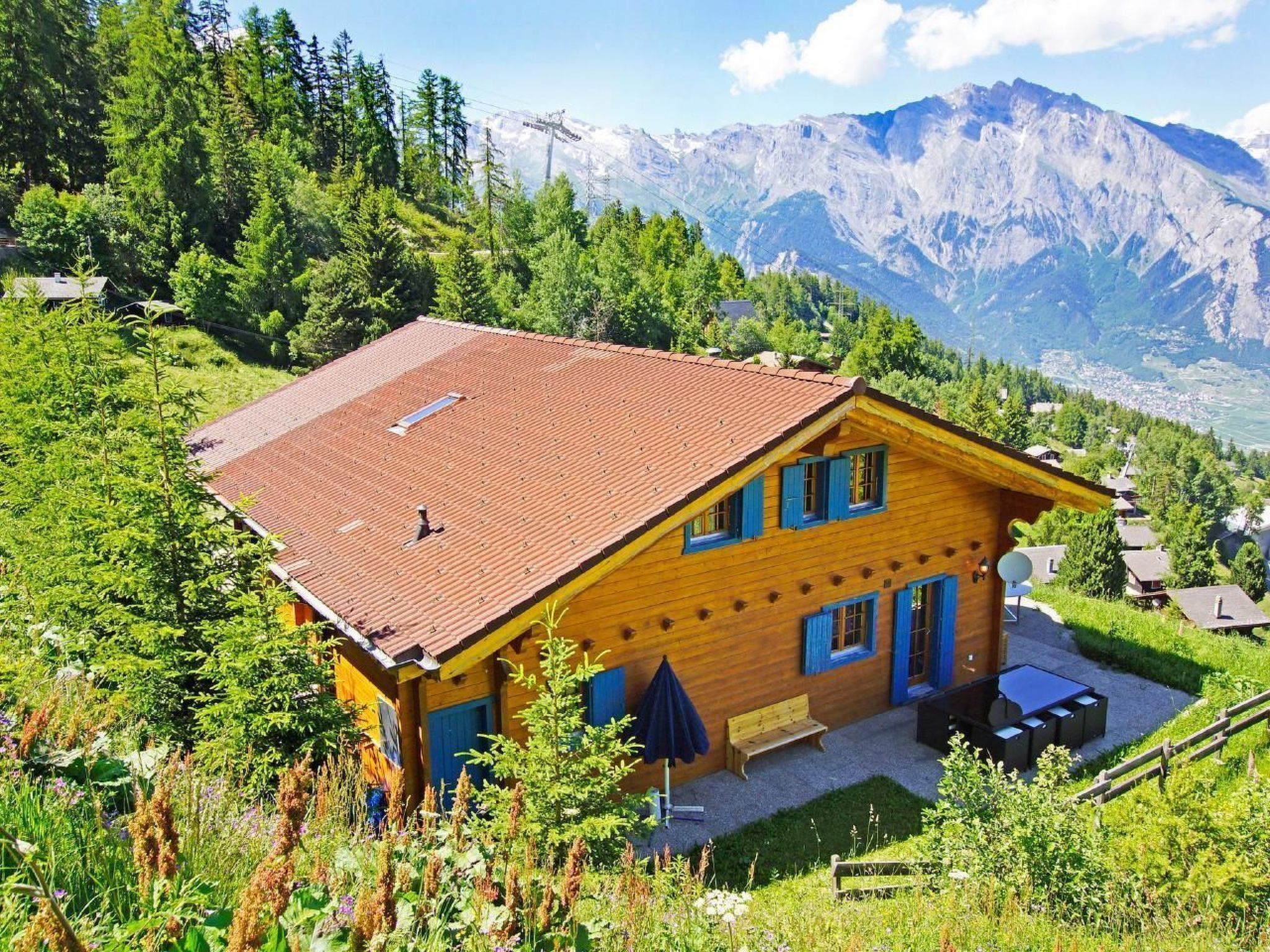 Eine Holzhütte mit rotem Dach, umgeben von üppiger Vegetation und Bergen im Hintergrund.