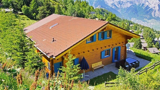 A wooden chalet with a red roof, surrounded by lush greenery and mountains in the background. - Chalet Alpina by Interhome (La Tzoumaz)