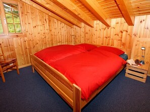 Ein Zimmer mit Holzboden, einem Bett, einem Sessel und einem Fenster.