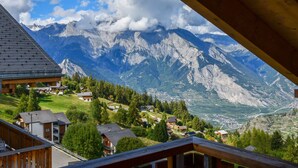 A mountain view from a wooden balcony overlooking a valley with houses and a clear sky. - Chalet Alpina by Interhome (La Tzoumaz)
