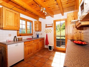 Eine Küche mit Holzschränken, einem Geschirrspüler, einem Waschbecken und einem Fenster mit Blick auf Grünflächen.
