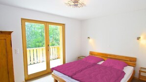 A bedroom with a wooden bed, a balcony door, and a small bedside table. - Chalet Chaud by Interhome (La Tzoumaz)
