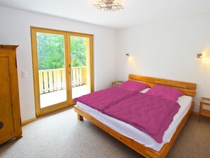 A bedroom with a wooden bed, a balcony door, and a small bedside table. - Chalet Chaud by Interhome (La Tzoumaz)