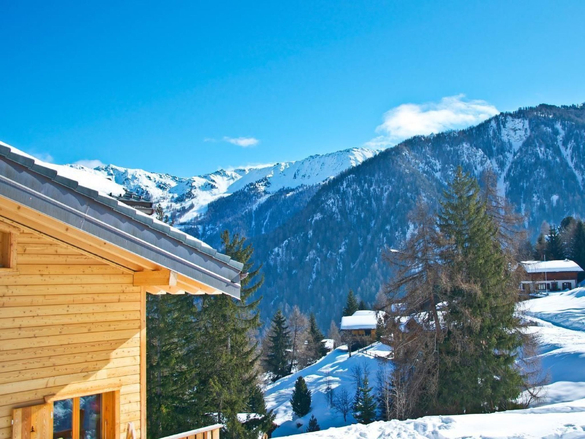 A wooden cabin with a view of snow-covered mountains and pine trees.