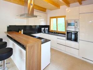 A modern kitchen with white cabinets, a wooden island, a built-in oven, and a window. - Chalet Chaud by Interhome (La Tzoumaz)