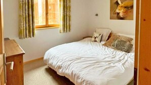 A bedroom with a bed, a wooden dresser, a window with curtains, and a wall-mounted picture. - Chalet Chaud by Interhome (La Tzoumaz)