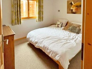 A bedroom with a bed, a wooden dresser, a window with curtains, and a wall-mounted picture. - Chalet Chaud by Interhome (La Tzoumaz)