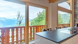 A modern kitchen with a large island, wooden balcony railing, and a view of mountains. - Chalet Harmonie by Interhome (La Tzoumaz)