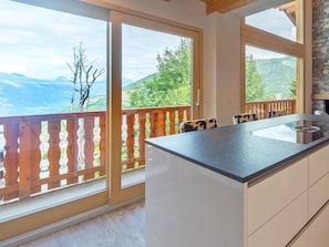 Eine moderne Küche mit einer großen Kochinsel, Holz-Balkonverkleidung und Blick auf Berge.